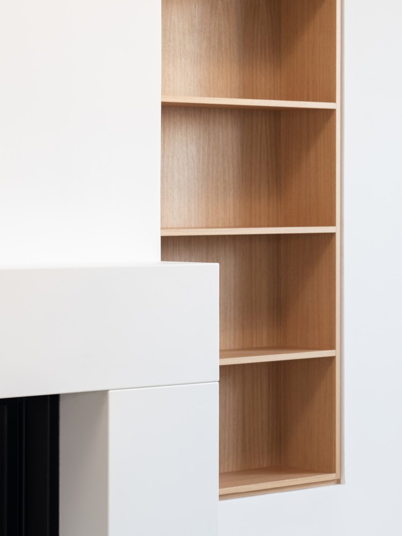 Kaminverkleidung in weiß lackiertem Metall und Bücherregal in Wandnische von Bonauer Bölling Architekten