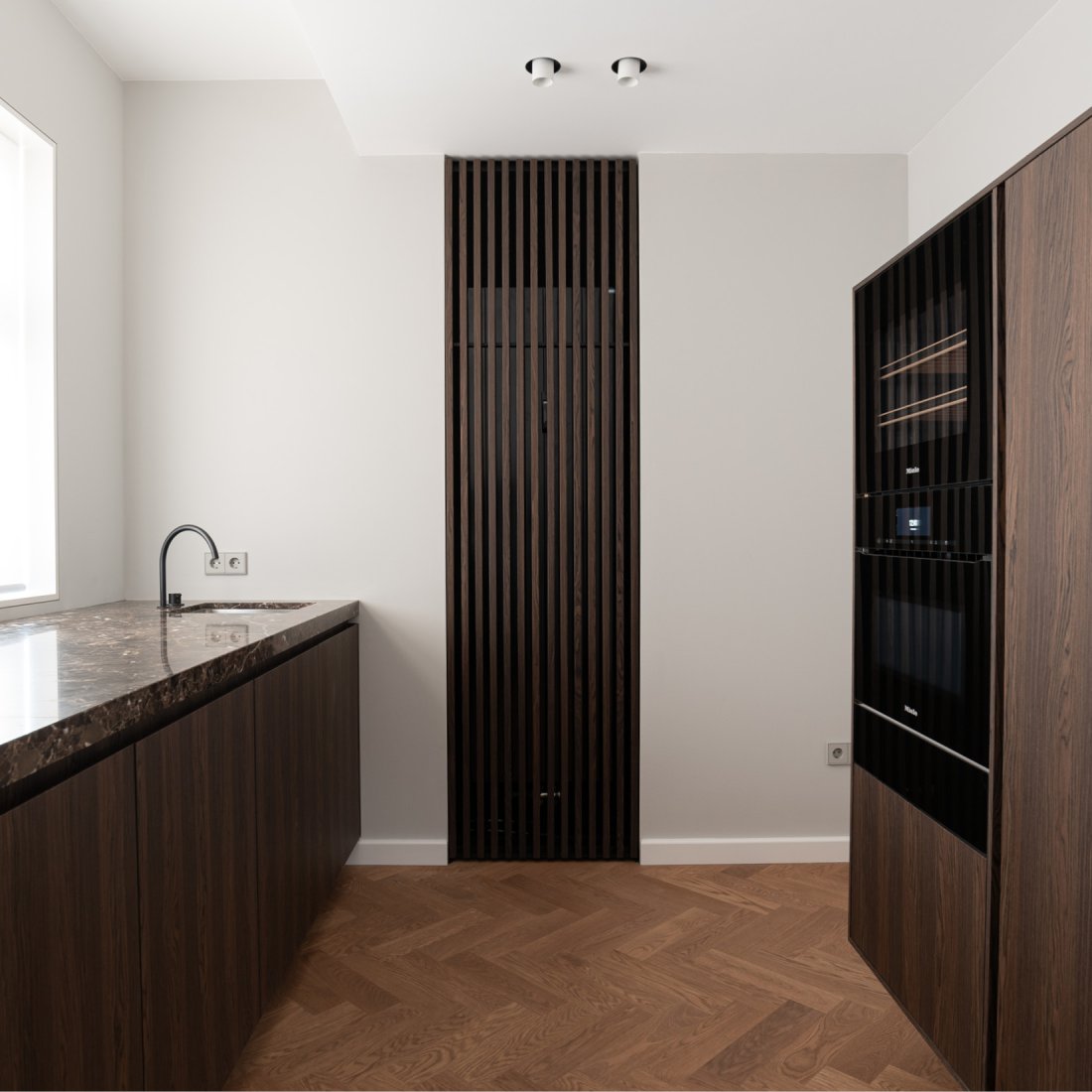 Maßgefertigte Einbauküche aus Räuchereiche. Marmorarbeitsplatte aus Emperador Marron mit schwarzer Vola Armatur. Vollintegrierte Miele Einbaugeräte Serie Artline.