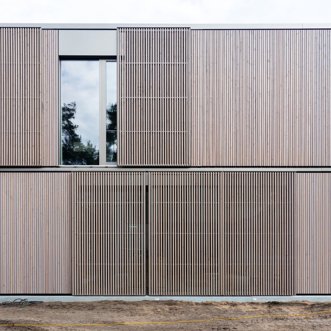 Detail der Holz-Aluminum-Fenster und der davor verlaufenden Schiebeläden aus vergrautem Lärchenholz