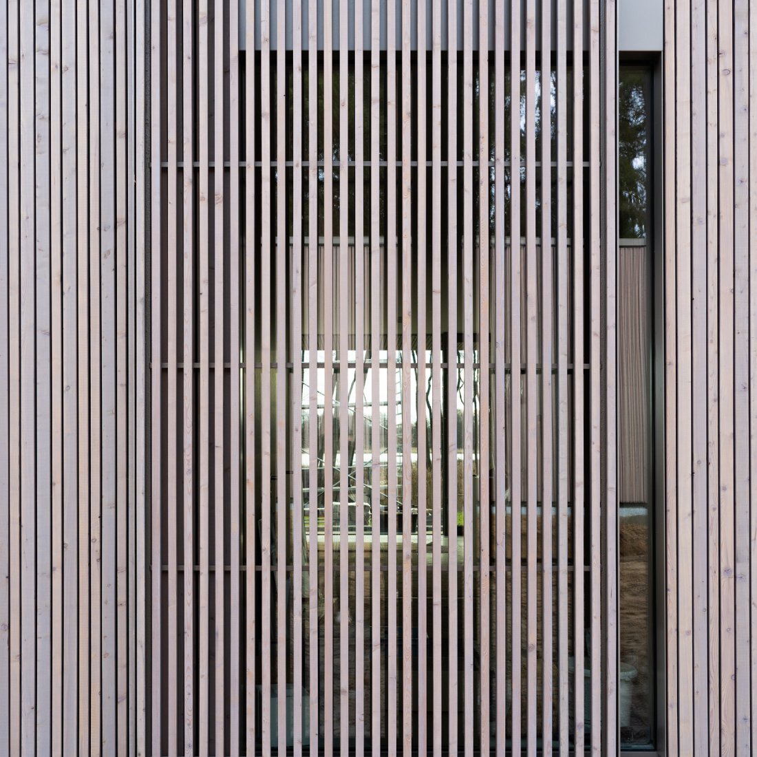 Detail der Holz-Aluminum-Fenster und der davor verlaufenden Schiebeläden aus vergrautem Lärchenholz