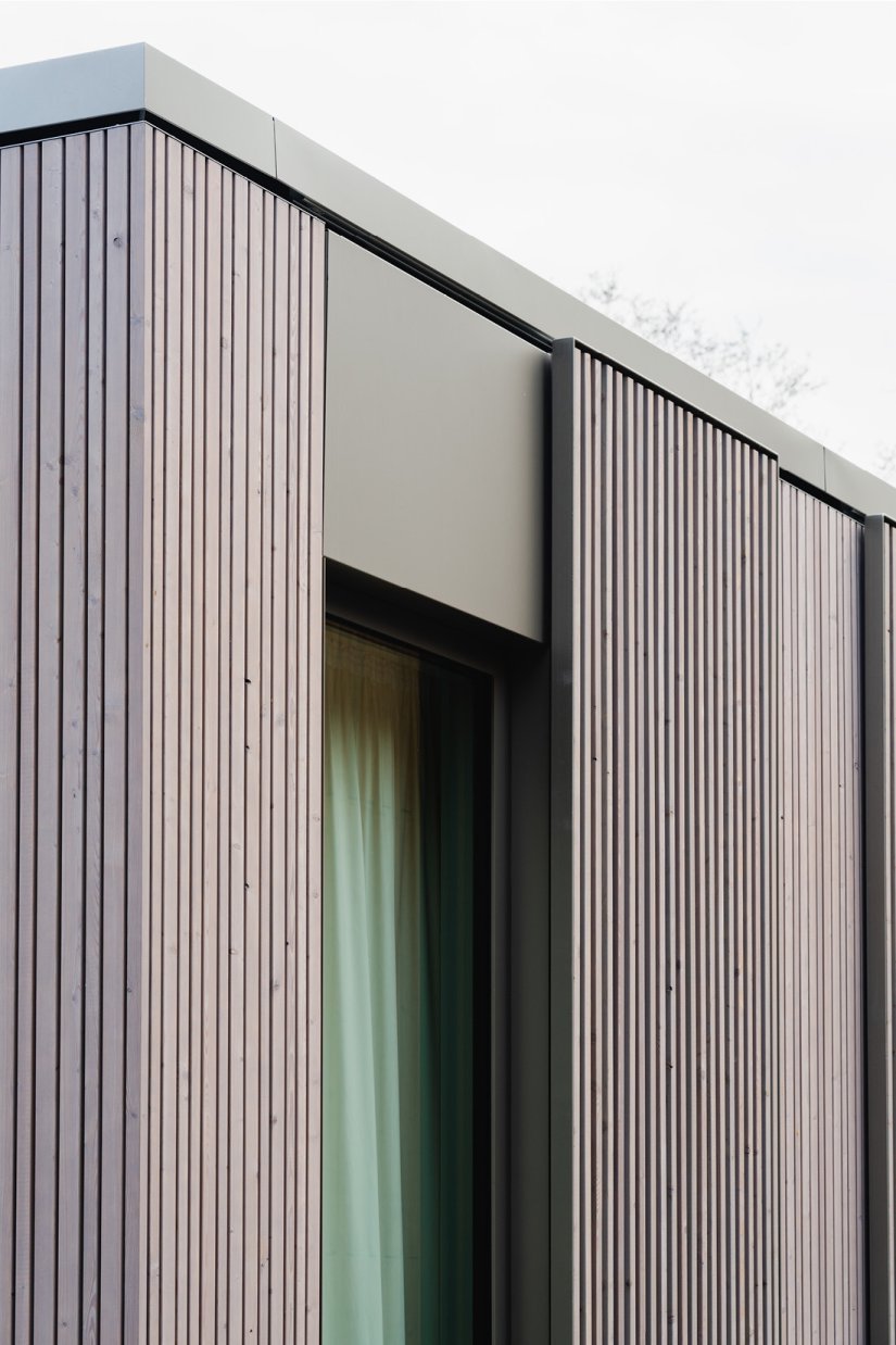 Detail der Holz-Aluminum-Fenster und der davor verlaufenden Schiebeläden aus vergrautem Lärchenholz