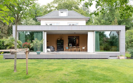 Wohnpavillion aus Sichtbeton mit vorvergrauer Holzfassade aus Lärche mit großzügiger Glasfassade und Hebe-Schiebeanlage zum Garten von Bonauer Bölling Architekten