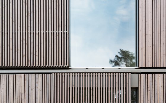 Detail der Holz-Aluminum-Fenster und der davor verlaufenden Schiebeläden aus vergrautem Lärchenholz